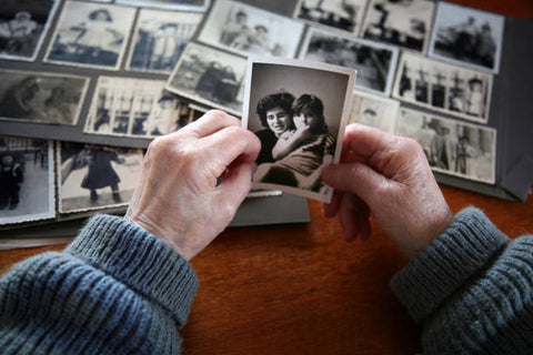 Elderly hands looking through old family photos on a wooden table